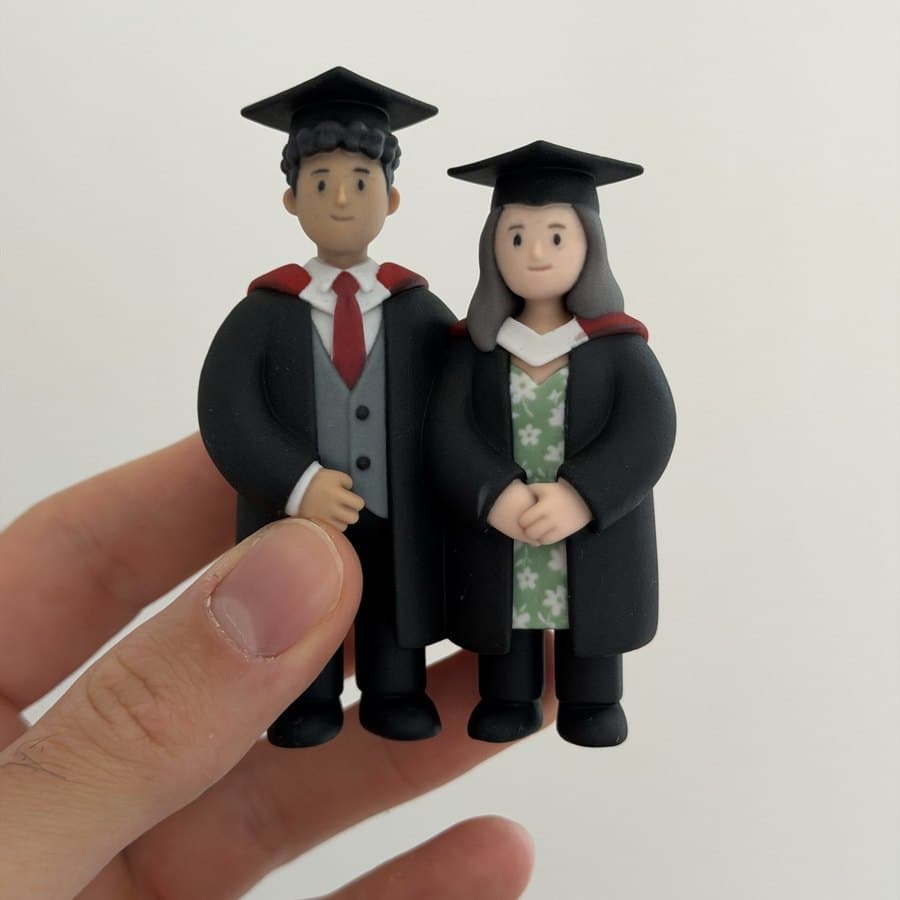 Two graduate figurines in caps and gowns held in a hand